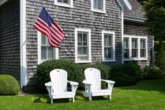2 adirondack chairs outside a house on a sunny day.