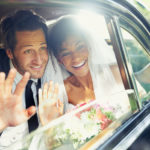 A newly married interracial couple waiving to people while in a car.