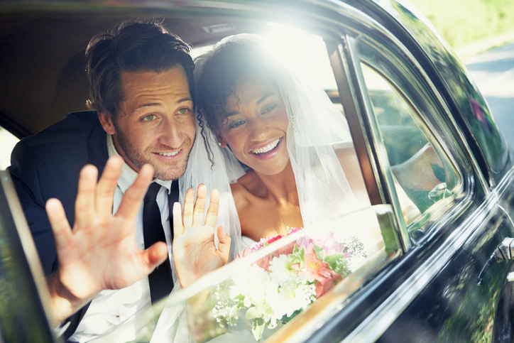 A newly married interracial couple waiving to people while in a car.